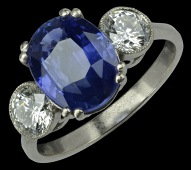 A sapphire and diamond three stone ring, the oval mixed-cut sapphire claw set between two millegrain collet set...