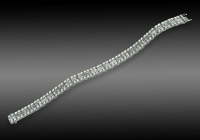 A diamond line bracelet, composed of articulated links, set with a central line of baguette-cut diamonds and outer...