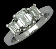 A three stone emerald-cut diamond ring, the three graduated emerald-cut diamonds claw set, platinum mounted, shank...