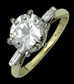 A solitaire diamond ring, the brilliant-cut diamond claw set between raised baguette-cut diamond shoulders, mounted...
