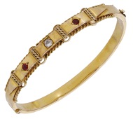 A late 19th century bangle, the front set with a reverse-mounted old brilliant-cut diamond and two circular-cut red...