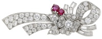 A ruby and diamond clip, circa 1950, the ribbon spray with applied flowerhead, set throughout with brilliant,...