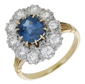 A sapphire and diamond cluster ring, the cushion-cut sapphire claw-set within a surround of brilliant-cut diamonds,...