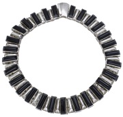 A silver and onyx collar necklace, composed of articulated convex panel links, alternately inset with...